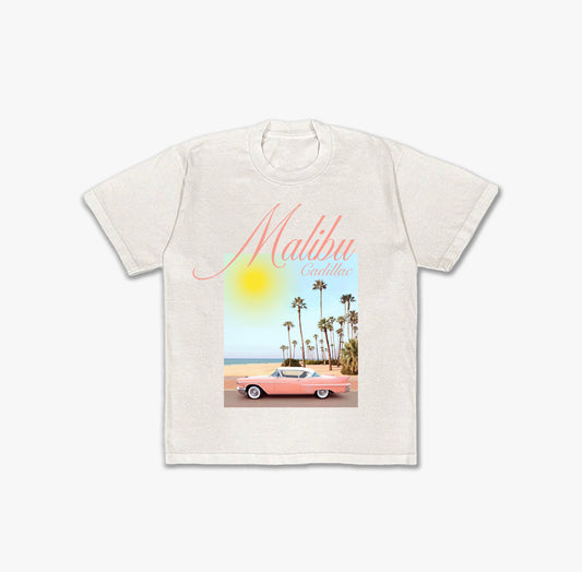 Off-white t-shirt featuring a graphic of a pink vintage Cadillac convertible parked on a coastal road with palm trees and a bright yellow sun, with 'Malibu Cadillac' text in pink script above.